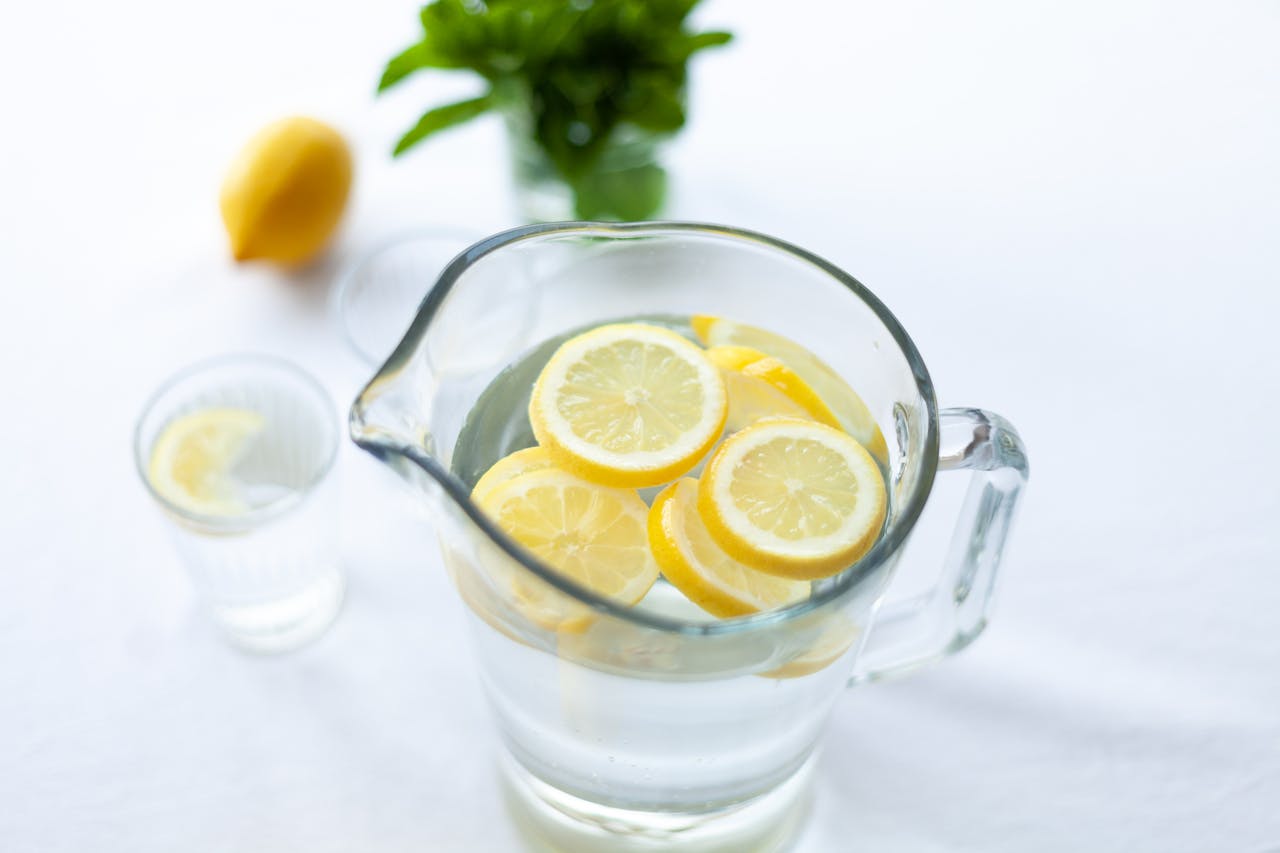 heros-img Top-down view of lemon slices in a glass pitcher filled with water, offering a refreshing drink option.